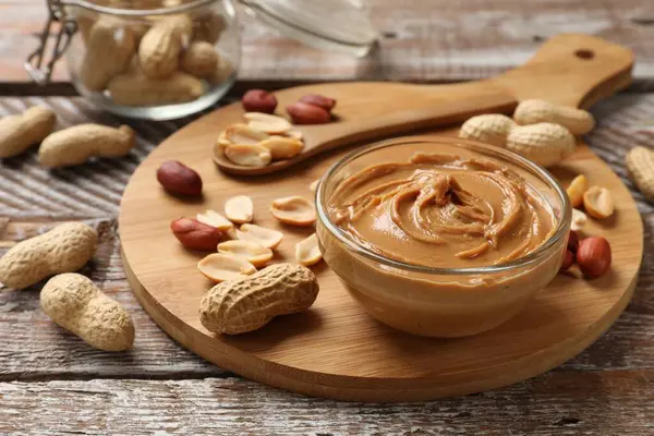 stock image Tasty peanut butter in bowl and groundnuts on wooden table