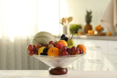 İçerideki beyaz masada farklı meyve ve böğürtlen içeren cam vazo