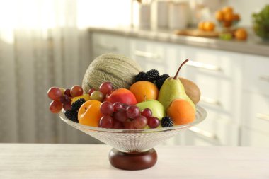 İçerideki beyaz masada farklı meyve ve böğürtlen içeren cam vazo