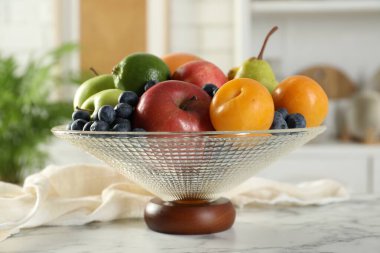 Beyaz mermer masanın üzerinde farklı taze meyveler bulunan cam vazo, yakın plan.