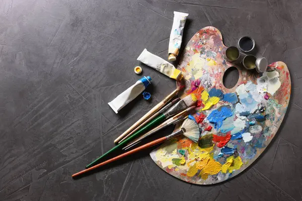 Sanatçı paleti, fırçalar ve boyalar gri masada, düz yerde. Metin için boşluk