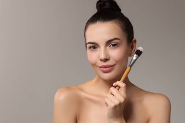 Güzel makyaj. Gri arkaplanda fırçası olan çekici kadın, metin için boşluk