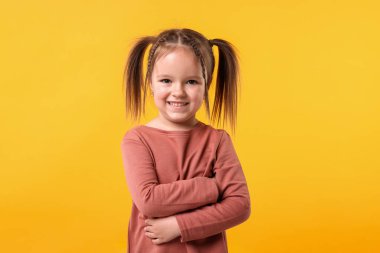 Turuncu arka planda çapraz kollu şirin küçük kız portresi.