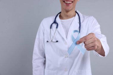 Prostat kanseri farkındalığı. Gri arkaplan ve seçici odak noktasında açık mavi kurdele tutan doktor