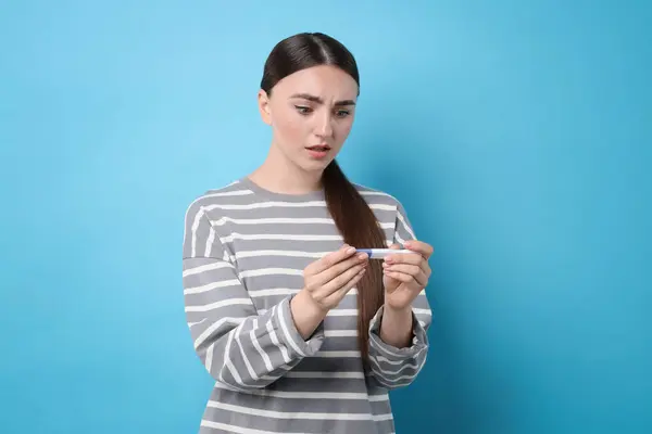 stock image Shocked woman holding pregnancy test on light blue background