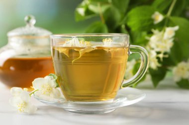 Aromatik yasemin çayı fincanda, çiçekler ve yeşil yapraklar beyaz masada