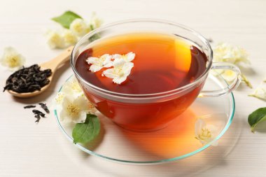 Sıcak yasemin çayı fincanda ve çiçekler beyaz ahşap masada.