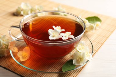 Sıcak yasemin çayı fincanda ve çiçekler beyaz ahşap masada.