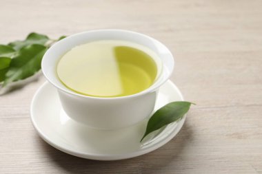 Yeşil çayı fincanda tazeleyen ve ahşap masada yapraklar, yakın plan