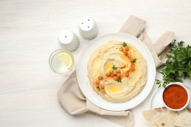 Beyaz ahşap masada servis edilen zeytinyağı, nohut ve kırmızı biber ile nefis bir humus.