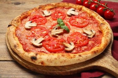 Domatesli, mantarlı ve ahşap masadaki fesleğenli lezzetli pizza.