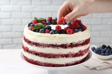 Lezzetli sünger keki beyaz masada böğürtlenlerle süsleyen kadın, yakın plan.