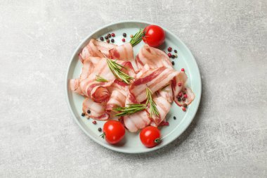 Açık gri masada çiğ domuz pastırması, baharat ve domates dilimleri.