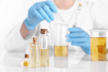 Aromaterapi ürünü. Laboratuvarda beyaz masada gerekli yağları üreten bilim adamı, şişelere odaklanıyor