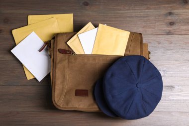 Kahverengi postacı çantası, zarflar, gazeteler ve şapka ahşap masanın üstünde.