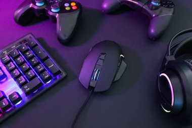 Bilgisayar faresi, kulaklık, RGB klavye ve oyun denetleyicileri koyu arkaplanda neon ışıkları, yakın plan