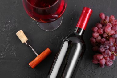 Tirbuşon, bir bardak şarap, siyah masada şarap ve üzüm.