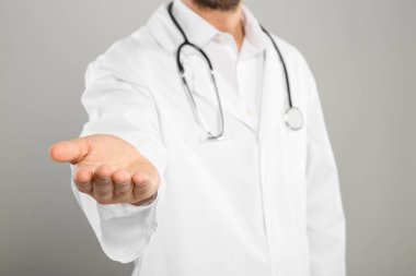 Steteskoplu bir doktor açık gri arka planda bir şey tutuyor, yakın plan.