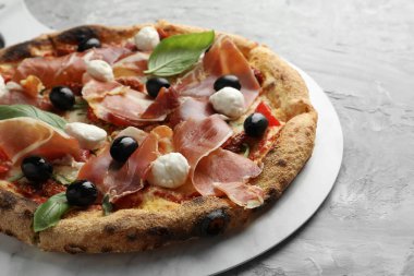 Pişmiş jambonlu, zeytinli, mozarella peynirli, güneşte kurutulmuş domates ve fesleğenli lezzetli pizza, yakın plan.