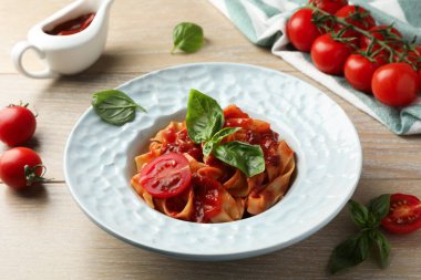 Soslu lezzetli makarna, domates ve fesleğen ahşap masada, yakın plan.