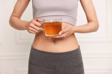 Kilo verme konsepti. Beyaz duvarın yanında diyet çayı içen kadın, yakın plan.