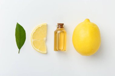 Beyaz arka planda bir şişe temel yağ, limon ve yeşil yaprak.