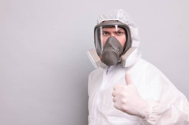 Koruyucu giysili ve solunum maskeli bir adam arka planda baş parmağını gösteriyor. Metin için boşluk
