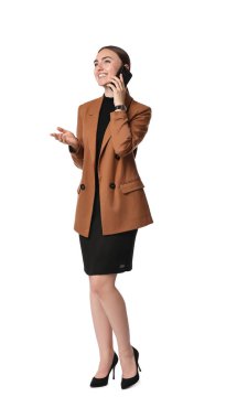Kahverengi ceketli ve siyah elbiseli güzel bir kadın beyaz arka planda akıllı telefondan konuşuyor.