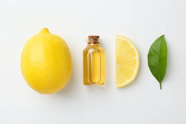 Beyaz arka planda bir şişe temel yağ, limon ve yeşil yaprak.