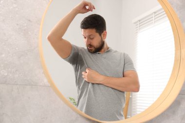 Evde aynanın yanında deodorant kullanmadan önce tişörtlü duygusal bir adam.