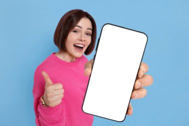 Açık mavi arka planda boş ekranlı cep telefonu gösteren mutlu bir kadın. Tasarım için model
