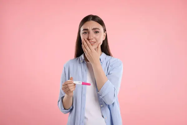 stock image Sad woman holding pregnancy test on pink background