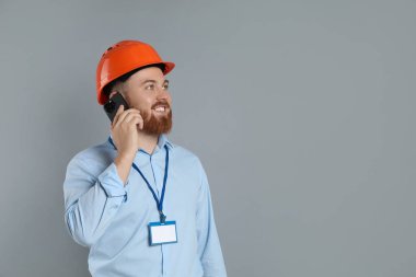 Sert şapkalı mühendis gri arkaplan ve metin için alan hakkında akıllı telefondan konuşuyor.
