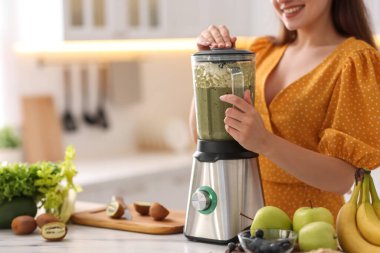 Genç bir kadın mutfaktaki beyaz mermer masada blender ile nefis smoothie yapıyor.