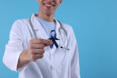 Prostat kanseri farkındalığı. Doktor elinde sahte bıyıklı mavi kurdele tutuyor. Renkli arka plan, seçici odaklanma. Metin için boşluk