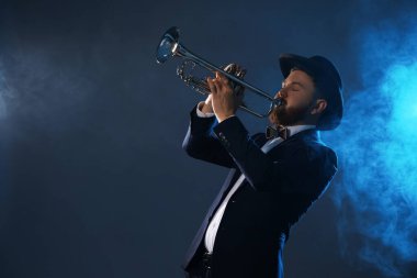 Professional musician playing trumpet on dark background in blue lights and smoke. Space for text clipart