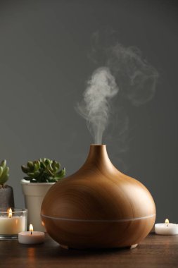 Aroma yağı yayıcı, ev bitkileri ve ahşap masada yanan mumlar.
