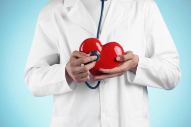 Steteskoplu doktor ve açık mavi arka planda kırmızı kalp, yakın plan.