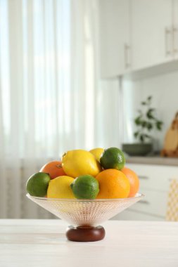 Beyaz masa üzerinde farklı narenciye meyveleri olan cam vazo.