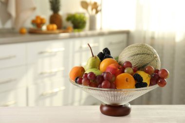 İçerideki beyaz masada farklı meyve ve böğürtlen içeren cam vazo