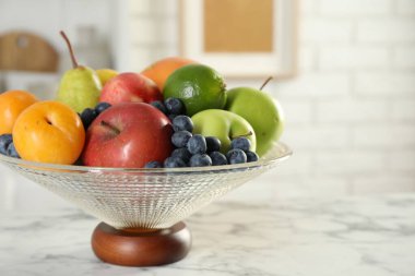 Beyaz mermer masanın üzerinde farklı taze meyveler bulunan cam vazo, yakın plan. Metin için boşluk