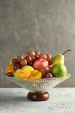 Gri dokuma masasında farklı taze meyveler bulunan cam vazo, metin için yer.