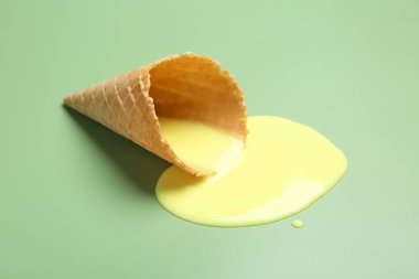 Açık yeşil zemin üzerinde erimiş dondurma ve gofret konisi