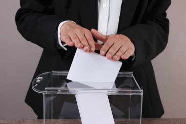 Kadın oyunu gri arka plandaki oy sandığına koyuyor, yakın plan.