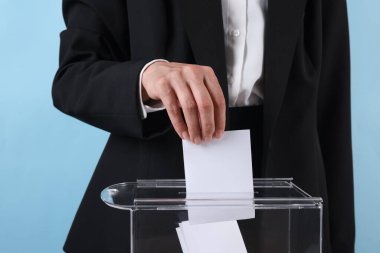 Kadın oyunu açık mavi arka plana karşı sandığa koyuyor, yakın plan.