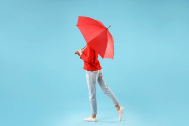Açık mavi arka planda kırmızı şemsiyeli kadın