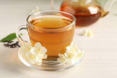 Sıcak yasemin çayı fincanda ve çiçekler beyaz ahşap masada.