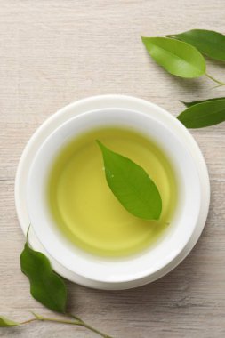 Yeşil çayı fincanda tazeleyip, ahşap masada yapraklar bırakarak, düz bir şekilde yatarak