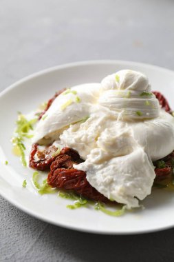 Nefis burrata peyniri ve açık gri masada kurutulmuş domatesler, yakın plan.