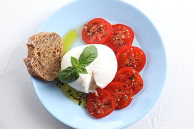 Lezzetli burrata peyniri, domates, fesleğen ve ekmek beyaz masada.